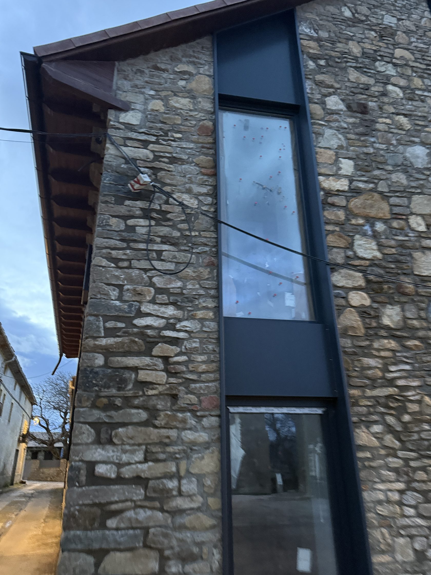 Detalle de ventanal con carpintería antracita sobre muro de piedra en Barós
